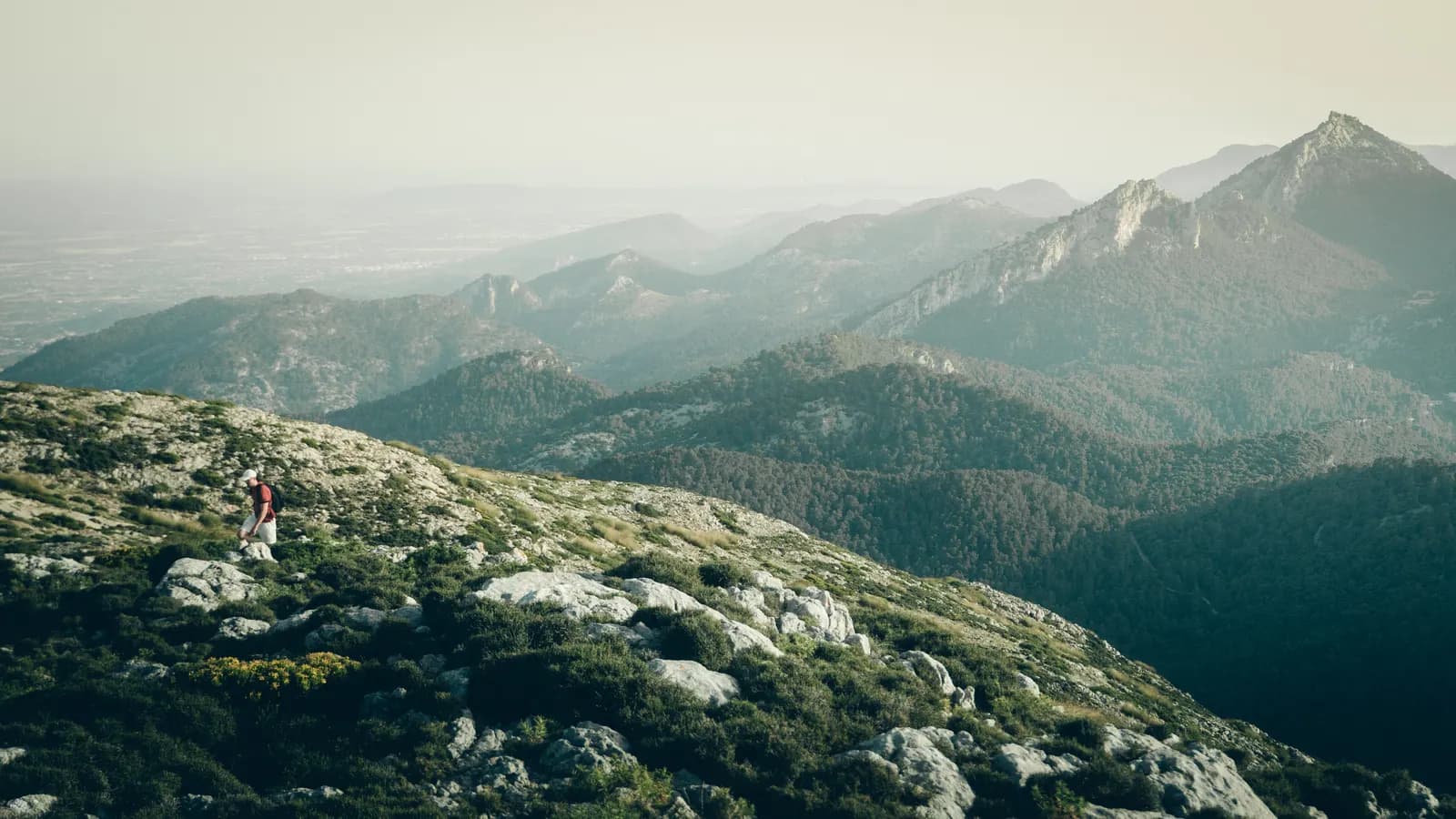 Weite Gebirgslandschaft auf Mallorca, auf dem Grat ein einzelner Wanderer.